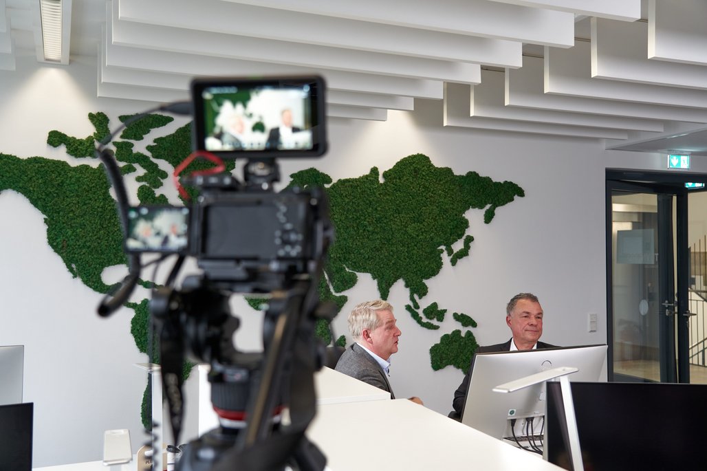 Boris Dombrowski und Knut Hirsch sitzen vor einer Wand mit der Weltkarte