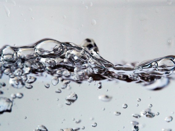 Nahaufnahme von spritzendem, klarem Wasser mit Luftblasen vor einem hellgrauen Hintergrund.