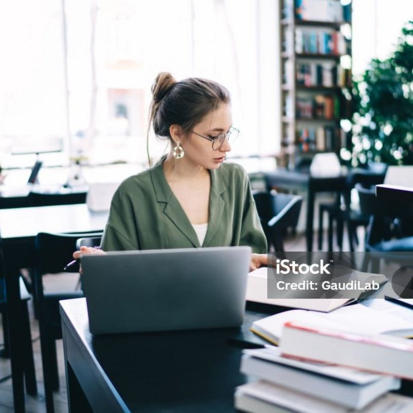 Studierende Frau in einer Bibliothek mit Notebook und Bücherstapel