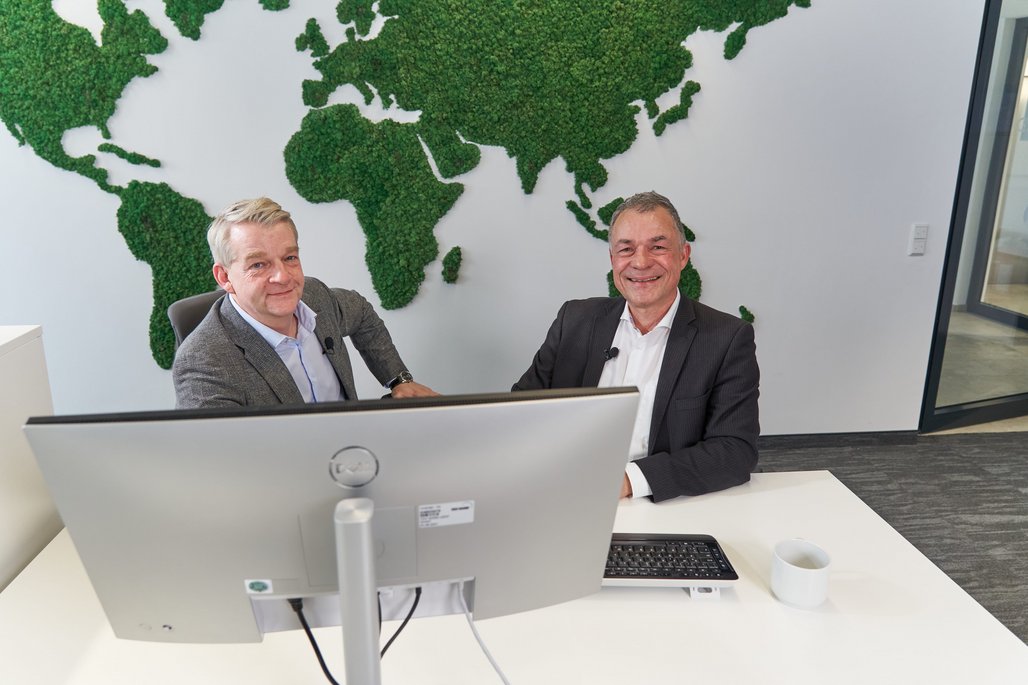 Boris Dombrowski und Knut Hirsch sitzen vor einer Wand mit der Weltkarte