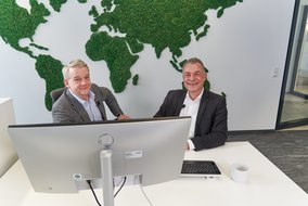 Boris Dombrowski und Knut Hirsch sitzen vor einer Wand mit der Weltkarte