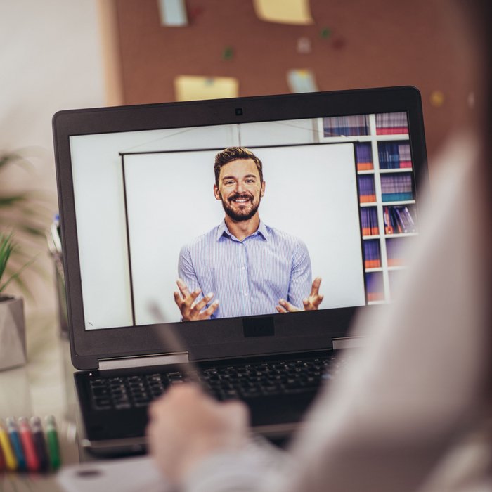 Symbolbild zum Thema Digital Expert Training: Eine Person sitzt vor ihrem Laptop. Auf dem Laptop ist ein Schulungsvideo mit einem Mann, der etwas erklärt, zu sehen.