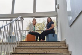Cherine Nickel und Natalie Morris im Treppenhaus auf Sitzhockern