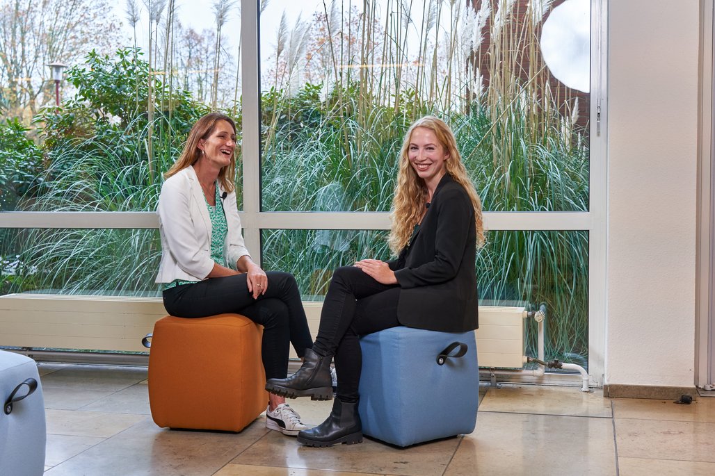 Alisha Gertack und Natalie Morris sitzen vor einer Fensterfront.