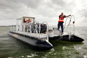 Mann steht auf Boot und wirft Kabel ins Wasser