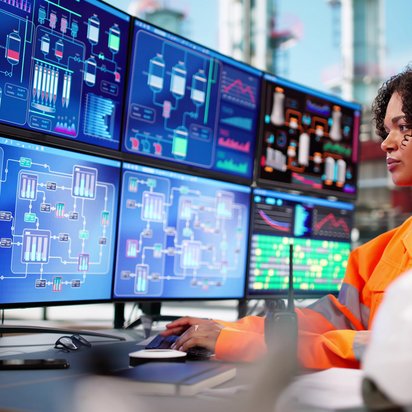 Symbolbild Sensoren, Transmitter, Messsysteme: Junge Ingenieurin sitzt vor einer Vielzahl an Monitoren, auf denen Überwachungsdaten eingespielt sind.