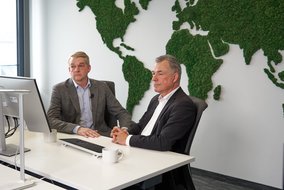 Boris Dombrowski und Knut Hirsch sitzen vor einer Wand mit der Weltkarte