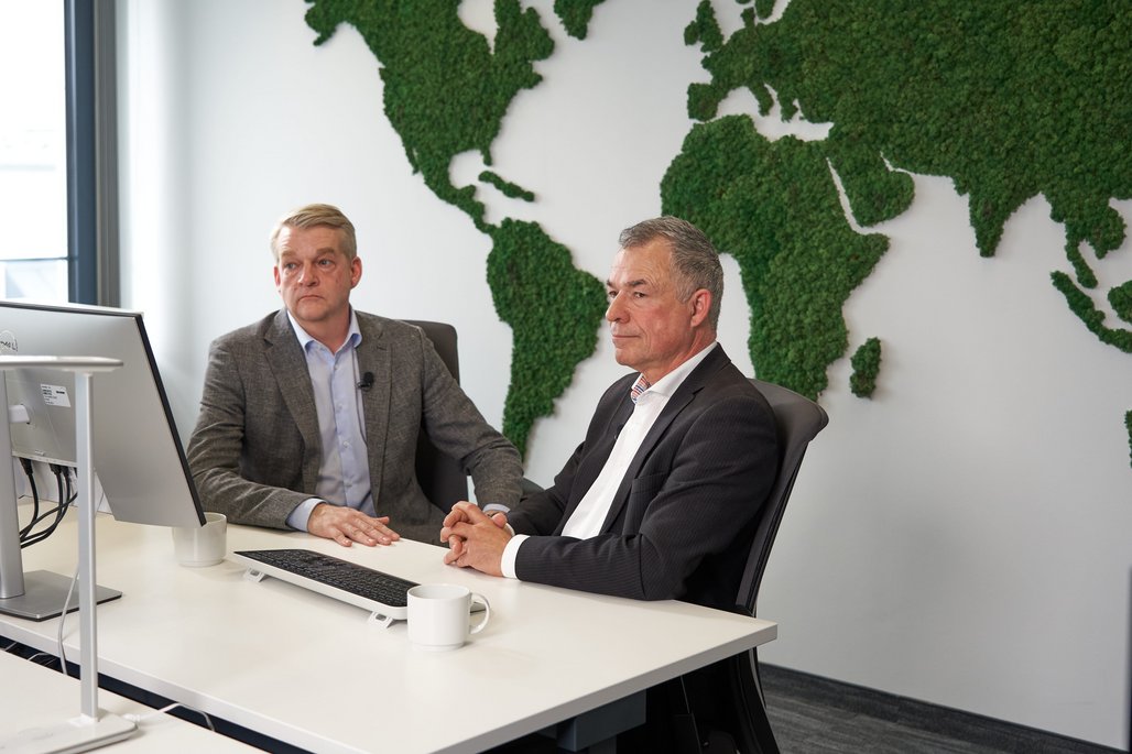 Boris Dombrowski und Knut Hirsch sitzen vor einer Wand mit der Weltkarte