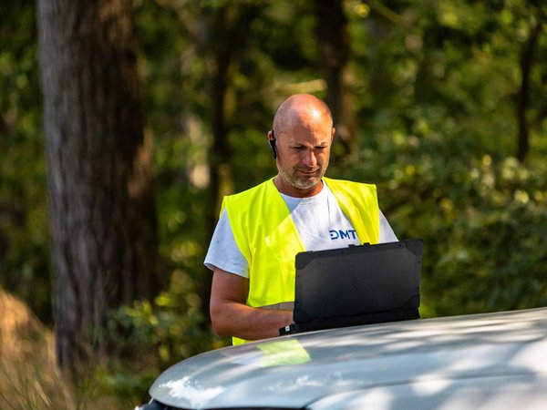 Ein Mitarbeiter der DMT-Seismik-Crew steht an einem Servicefahrzeug und nutzt einen Laptop