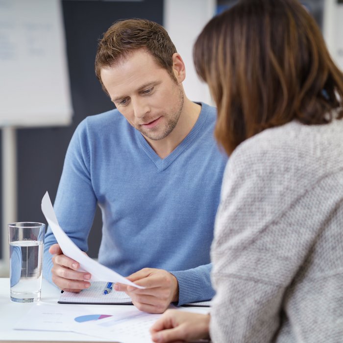 Symbolbild zum Thema Jobsharing: Eine Frau und ein Mann sitzen gemeinsam an einem Tisch. Der Mann hält Zettel in der Hand. Beide schauen darauf.