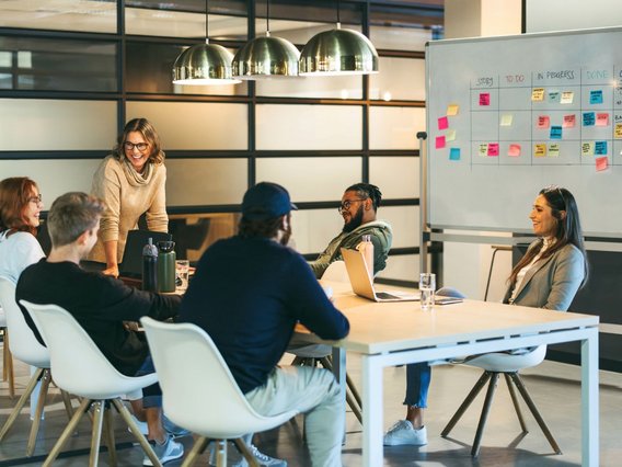 Büro_Workshop Fünf Personen sitzen und stehen um einen Tisch in einem modernen Büro.