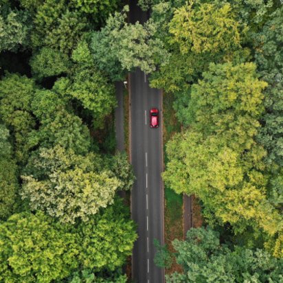 Klimaneutrale Mobilität Symbolbild für die Seite Klimaneutrale Mobilität: Bild aus Vogelperspektive, das ein Auto zeigt, das auf einer Landstraße durch einen grünen Wald fährt.