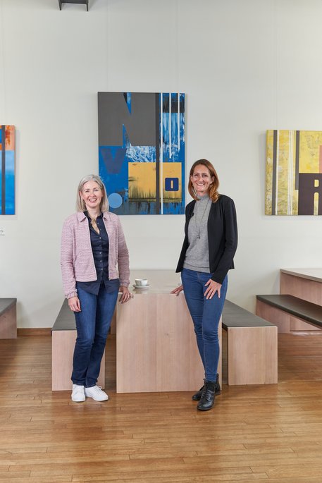 Mary Anderson und Natalie Morris stehen vor einem Tisch mit zwei Bänken