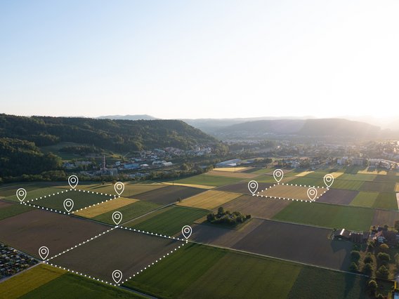 Symbolbild zum Thema Beteiligten- und Eigentümerrecherche: Auf einem Luftbild einer Feldflur sind virtuell mit Location-Markern Flurstücke markiert.