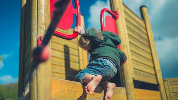 Kinderbetreuung Ein kleines Kind klettert auf ein hölzernes Gerüst auf dem Spielplatz.