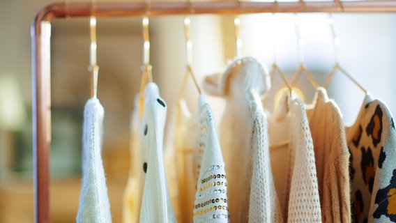 Kleidung Verschiedene Pullover und Strickjacken hängen auf Bügeln an einer Kleiderstange.