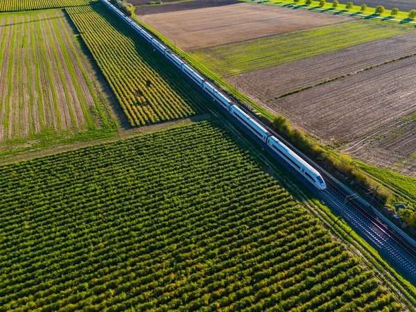 Symbolbild für Flächenmanagement für lineare Infrastruktur: Bahnstrecke mit ICE-Zug, umgeben von grünen Feldern