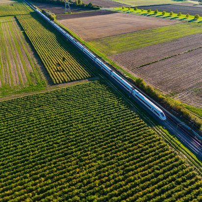 Symbolbild für Flächenmanagement für lineare Infrastruktur: Bahnstrecke mit ICE-Zug, umgeben von grünen Feldern