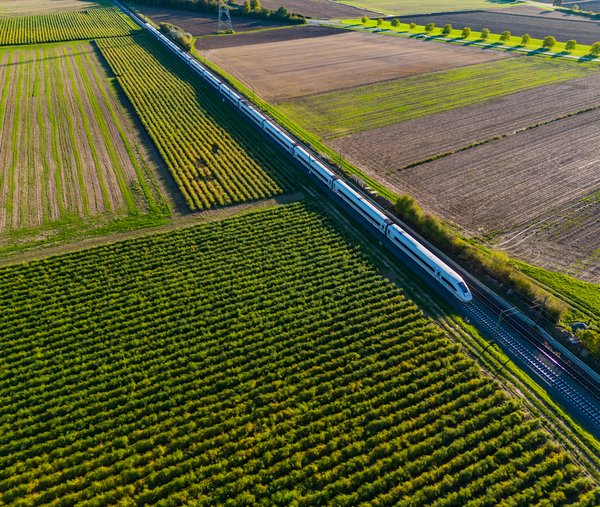 Symbolbild für Flächenmanagement für lineare Infrastruktur: Bahnstrecke mit ICE-Zug, umgeben von grünen Feldern