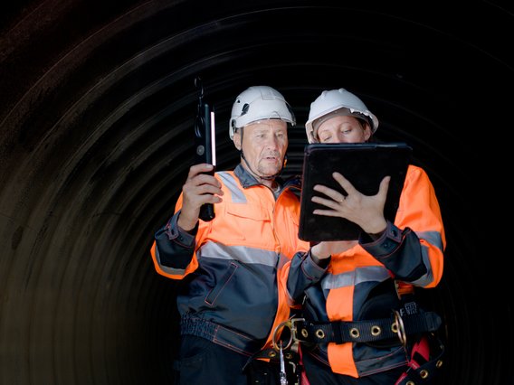 Zwei Ingenieure in einem Tunnel unter Tage überprüfen im Rahmen einer Sicherheitsprüfung die Notfallprotokolle.