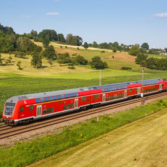 Bahntrasse mit einer fahrenden Regionalbahn in grüner Feldlandschaft 