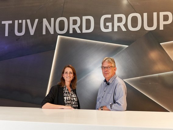 Rüdiger Misiek Rüdiger Misiek und Natalie Morris hinter einem Tresen. Hinter ihnen ist der Schriftzug TÜV NORD GROUP an der Wand zu sehen.