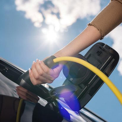 Nahaufnahme einer Hand, die ein gelbes Ladekabel an ein schwarzes Elektroauto anschließt. 