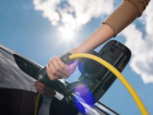 Nahaufnahme einer Hand, die ein gelbes Ladekabel an ein schwarzes Elektroauto anschließt. 