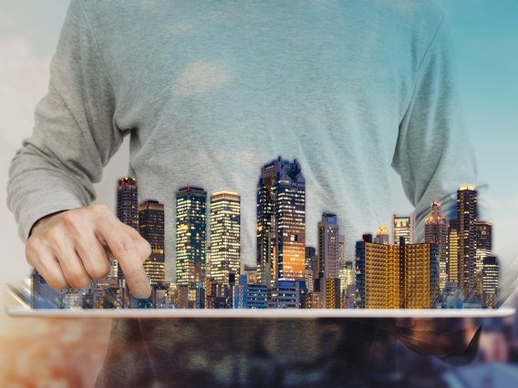 Symbolbild für den Bereich Immobilien: ein Hologramm einer Stadt mit Wolkenkratzern schwebt vor dem Torso eines Mannes, der sie zu bearbeiten scheint. 