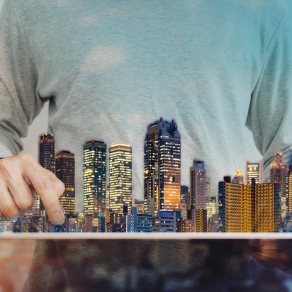 Symbolbild für den Bereich Immobilien: ein Hologramm einer Stadt mit Wolkenkratzern schwebt vor dem Torso eines Mannes, der sie zu bearbeiten scheint. 