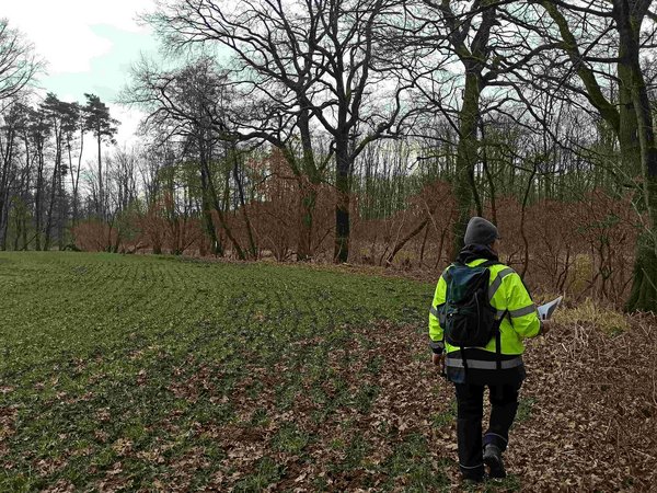 DMT-Umweltfachplanende im Einsatz: Eine Frau auf einem herbstlichen Feld mit Warnweste und Clipboard