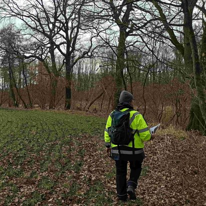 DMT-Umweltfachplanende im Einsatz: Eine Frau auf einem herbstlichen Feld mit Warnweste und Clipboard