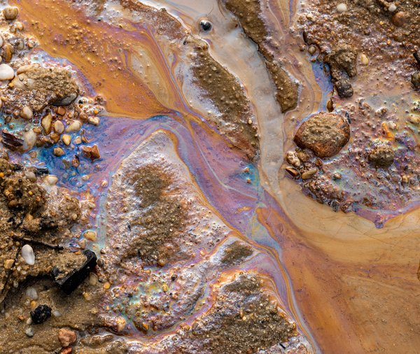 Ölverschmutzung im Wasser und auf dem Sand. Fossile Brennstoffe in der Umwelt. Spektralfarben des Lichts sind sichtbar. Die Natur ist durch Industrieabfälle kontaminiert.