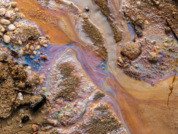 Ölverschmutzung im Wasser und auf dem Sand. Fossile Brennstoffe in der Umwelt. Spektralfarben des Lichts sind sichtbar. Die Natur ist durch Industrieabfälle kontaminiert.