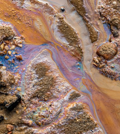 Ölverschmutzung im Wasser und auf dem Sand. Fossile Brennstoffe in der Umwelt. Spektralfarben des Lichts sind sichtbar. Die Natur ist durch Industrieabfälle kontaminiert.