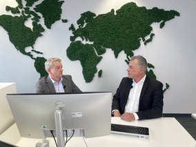 Boris Dombrowski und Knut Hirsch sitzen vor einer Wand mit der Weltkarte
