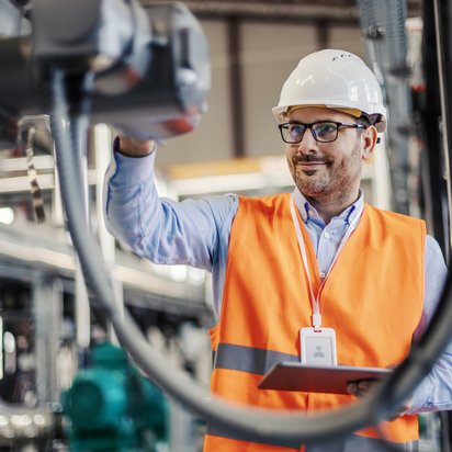 Monitoring von Maschinen und Anlagen Ein Ingenieur mit Schutzhelm prüft eine Maschine in einer Fabrik