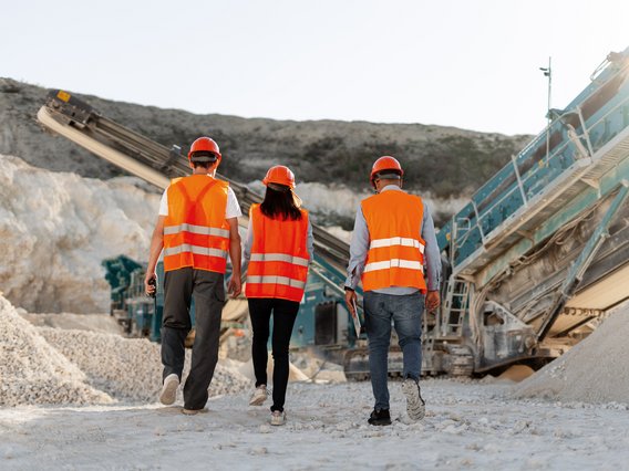 Scoping und Machbarkeitsstudien Symbolbild Scoping und Machbarkeitsstudien: Gruppe von drei Ingenieuren mit Helmen, die ein offenes Bergbauprojekt inspizieren