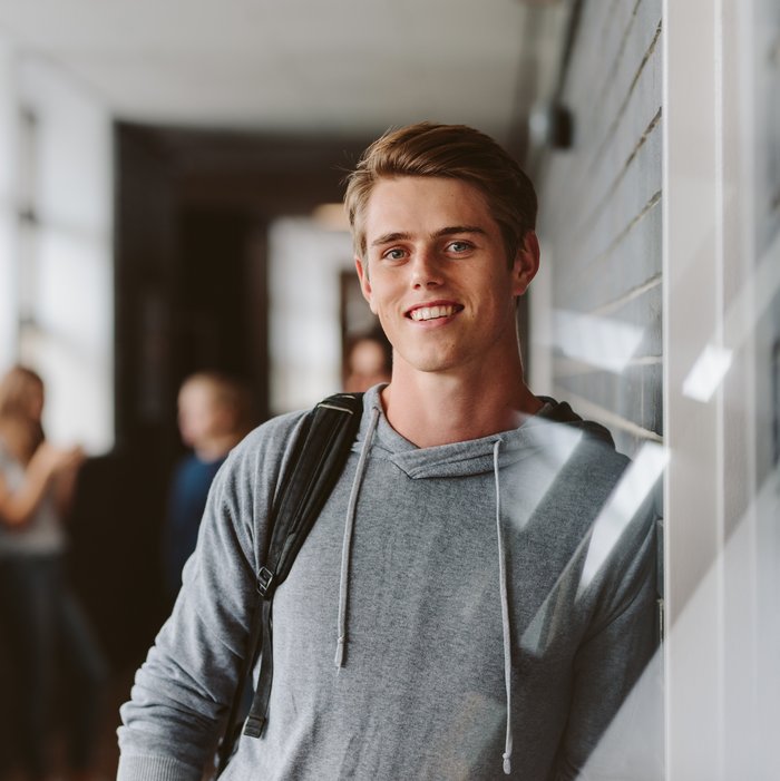 Junger Student in grauem Hoodie lehnt an einer Wand