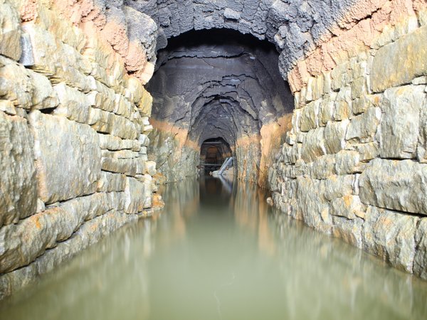 Blick in einen wassergefüllten Altbergbaustollen, das Wasser steht etwa bis zu einer Höhe von einem Meter.