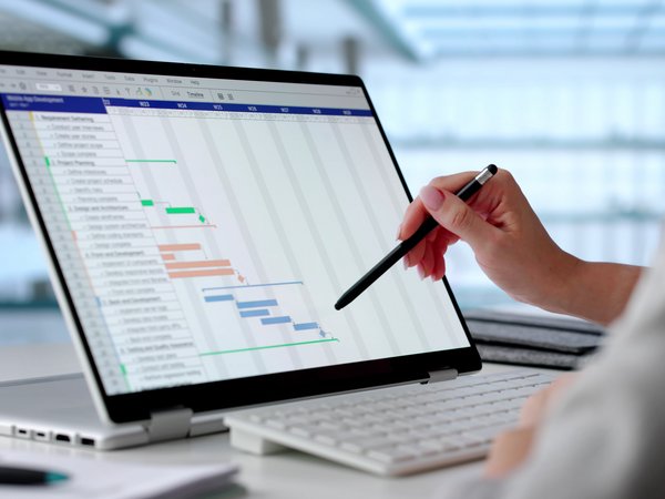Projektplanung am Notebook Symbolbild Projektplanung: Hände einer Person bedienen ein Interface auf einem digitalen Gerät, das auf einem Tisch vor ihr steht.