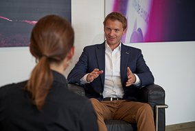 Roman Krähling und Natalie Morris sitzen vor einer Wand in Sesseln.