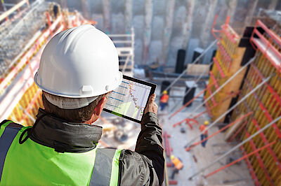Worker at a building site looking at data on a mobile device | DMT GROUP Worker at a building site looking at data on a mobile device | DMT GROUP